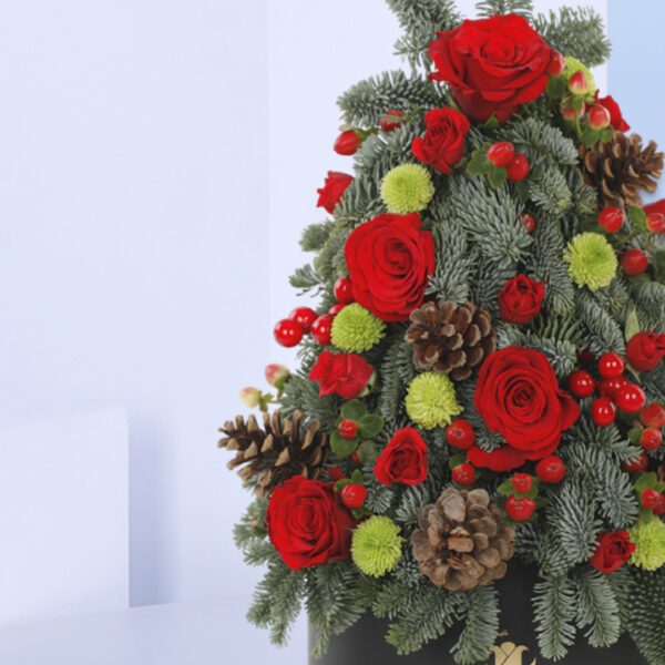 A Christmas tree-shaped floral arrangement in a black pot. The arrangement features red roses, green foliage, pine cones, and berries.