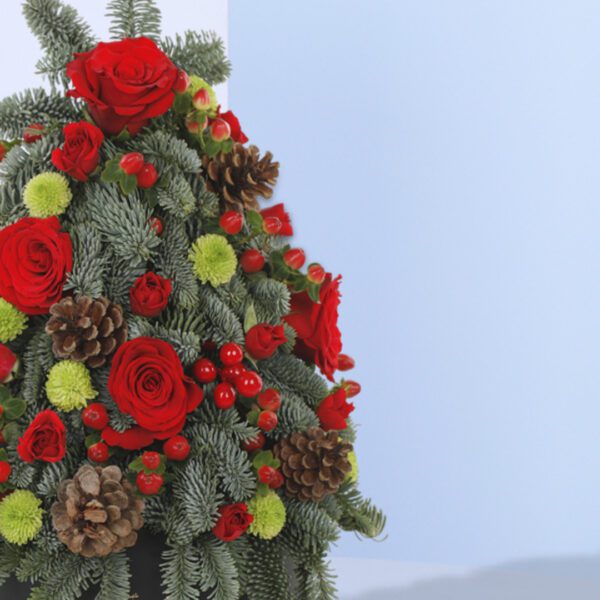 A Christmas tree-shaped floral arrangement in a black pot. The arrangement features red roses, green foliage, pine cones, and berries.