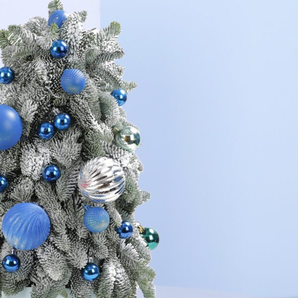 A small, frosted Christmas tree decorated with blue and silver ornaments. The tree is in a white pot and sits on a blue background.