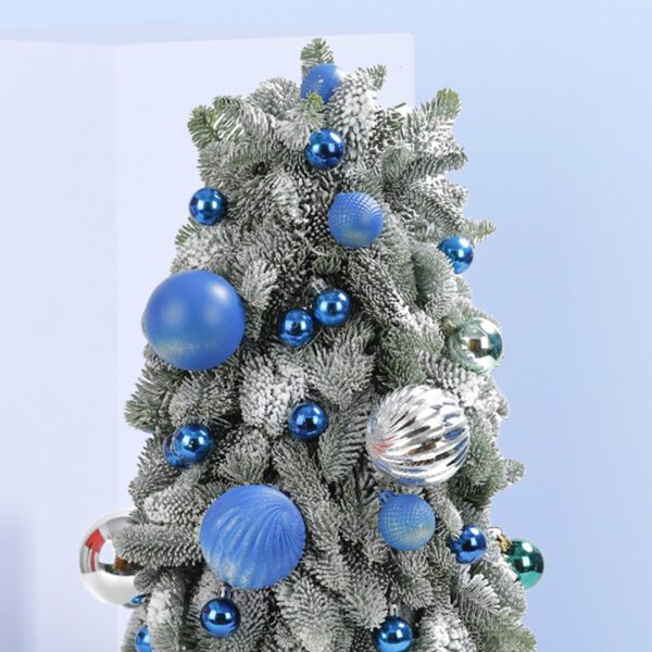 A small, frosted Christmas tree decorated with blue and silver ornaments. The tree is in a white pot and sits on a blue background.