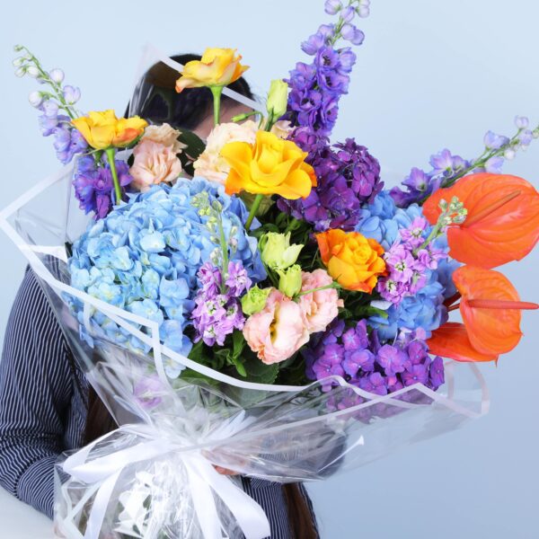 Exquisite bouquet of hydrangeas, Anthurium, peach Lisianthus, roses, and Delphinium, elegantly wrapped in glass sheet.