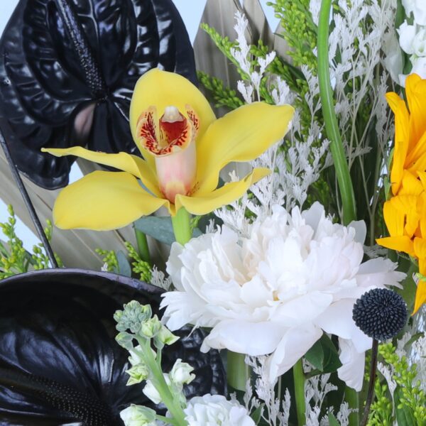 Bright sunflowers paired with striking black foliage, artfully presented on a pedestal.