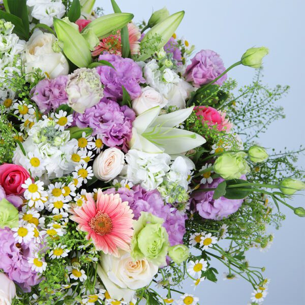 Colorful floral arrangement featuring pink gerberas, pink roses, white ohara lilies, and other mixed flowers in a glass vase.