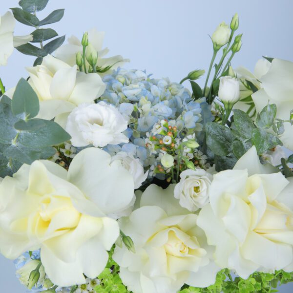 A vibrant arrangement of white roses, blue and green hydrangeas, and lisianthus, elegantly displayed with eucalyptus in a clear glass vase.