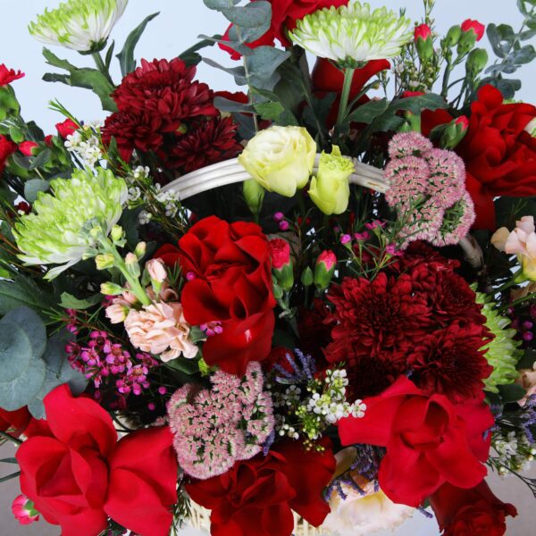 A charming basket overflowing with flowers, including roses, carnations, lisianthus, wax flowers, and eucalyptus.