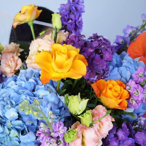 Stunning floral arrangement of hydrangeas, Anthurium, peach Lisianthus, and roses, beautifully wrapped in glass sheet.