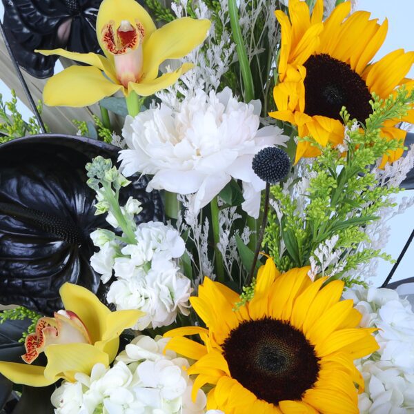 A vibrant sunflower bouquet with dramatic black leaves elegantly displayed on a pedestal.