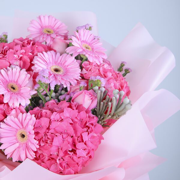 A vibrant pink bouquet with 5 gerberas, 5 hydrangeas, 5 pink roses, and ferns, wrapped in pink tissue paper and tied with a white ribbon.