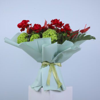 A vibrant bouquet of red roses, anthurium, and green hydrangea wrapped in light blue paper.