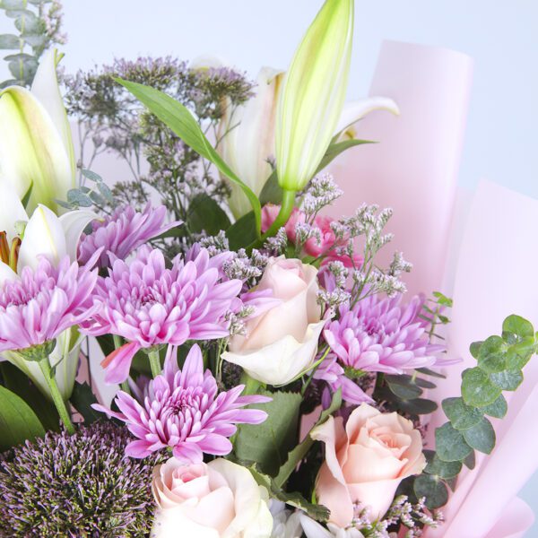 Mixed flowers arranged elegantly in a soft pink floral wrap, creating a lovely display.