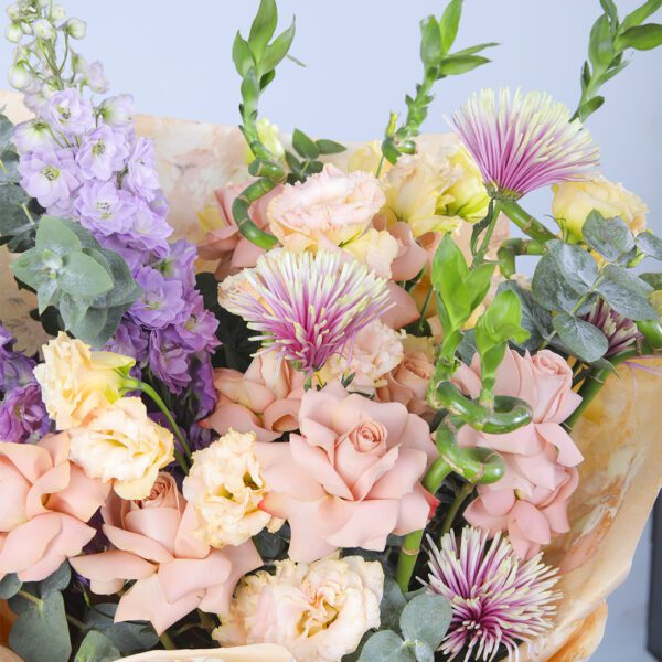 A stunning arrangement showcasing the delicate beauty of peach roses, the vibrant hues of delphinium, and the lushness of greenery.