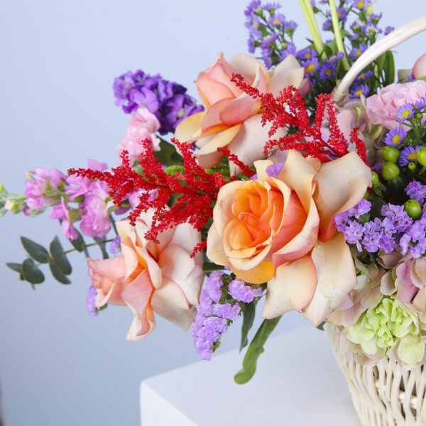 A delightful basket of pastel-hued flowers, showcasing hydrangeas, roses, and carnations, nestled among lush greenery.