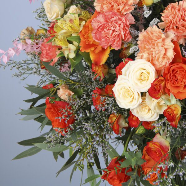 A vase filled with a mix of flowers including orange and pink carnations, garden roses, dianthus, and cream buttercups.