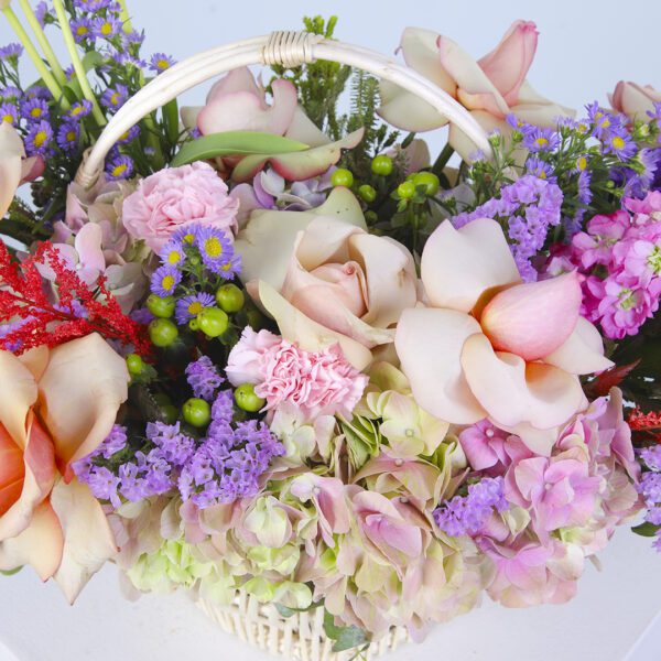 A basket overflowing with pastel-coloured flowers, featuring hydrangeas, roses, and carnations, surrounded by greenery.