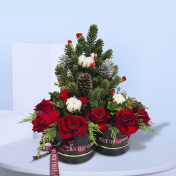 Two black gift boxes of Christmas floral arrangement with red roses, evergreen branches, pinecones, and cotton stems .