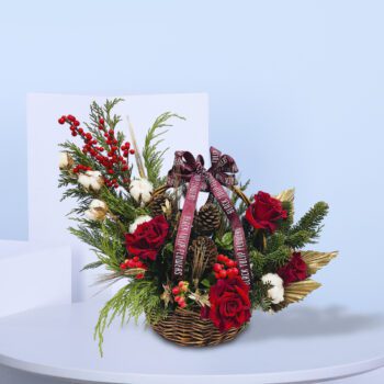 Christmas floral basket with red roses, pinecones, evergreens, berries, and cotton stems, tied with a festive ribbon.