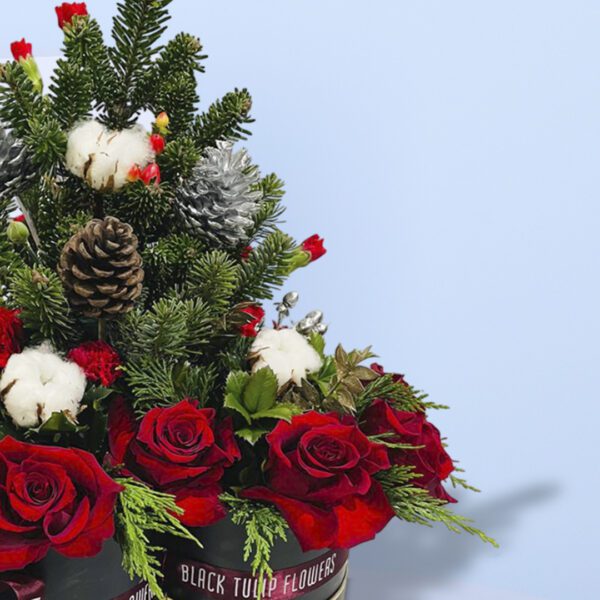 Two black gift boxes of Christmas floral arrangement with red roses, evergreen branches, pinecones, and cotton stems .