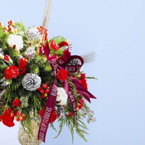 Red roses, pinecones, evergreens, and cotton stems in a golden transparent vase