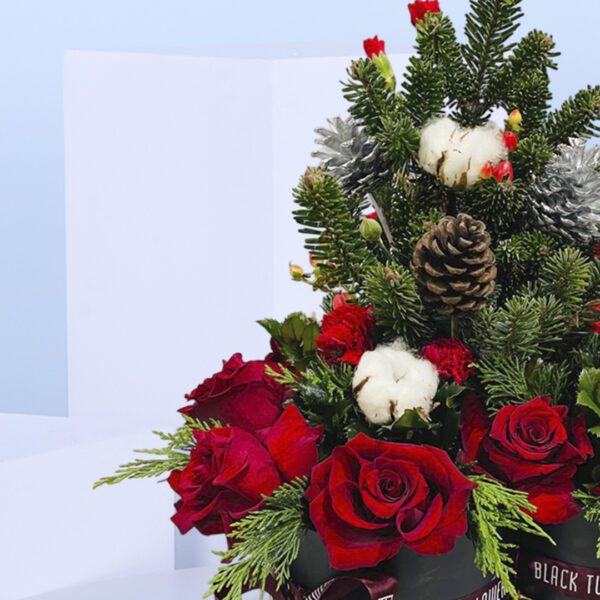 Two black gift boxes of Christmas floral arrangement with red roses, evergreen branches, pinecones, and cotton stems .