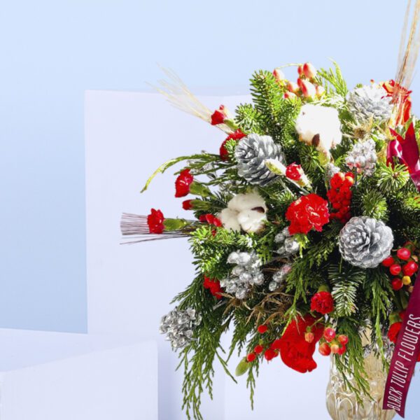 Red roses, pinecones, evergreens, and cotton stems in a golden transparent vase