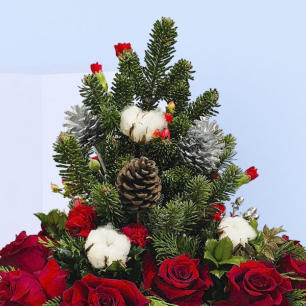 Two black gift boxes of Christmas floral arrangement with red roses, evergreen branches, pinecones, and cotton stems .