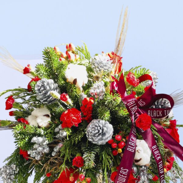 Red roses, pinecones, evergreens, and cotton stems in a golden transparent vase