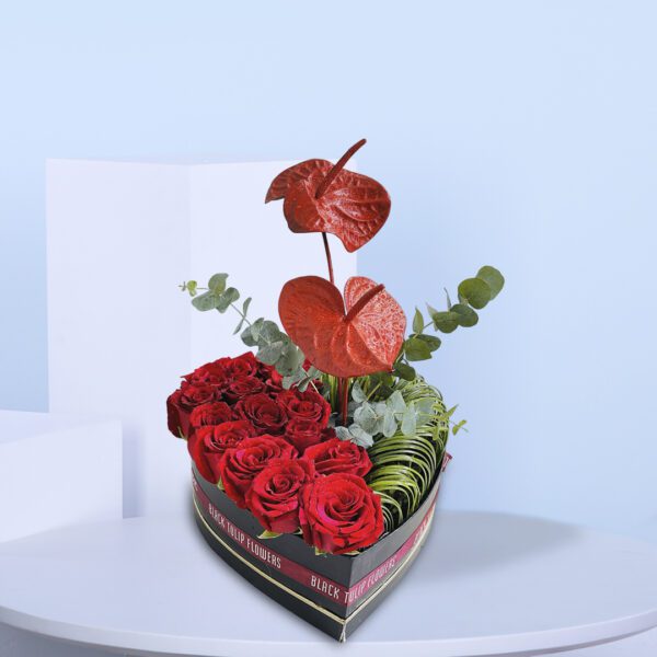 A heart-shaped box filled with red roses and anthuriums, symbolizing love and passion.