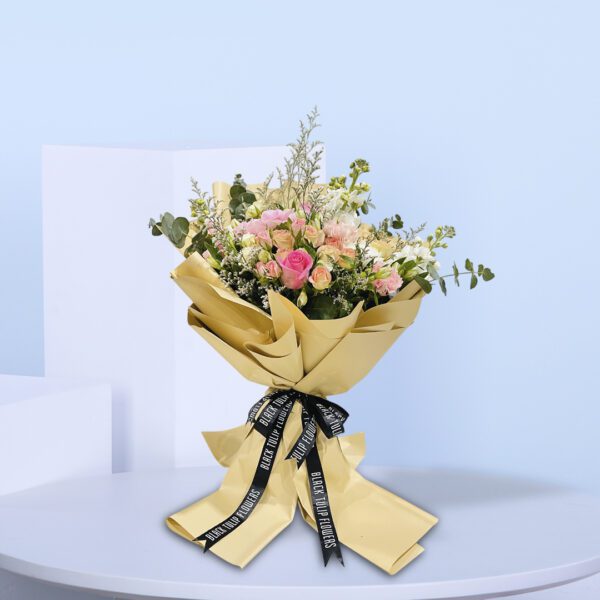 A bouquet of peach and pink roses in a light brown wrap tied with a black ribbon.