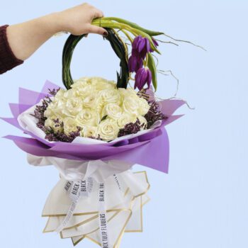 A beautiful arrangement of white roses and purple tulips in a basket with a unique handle.