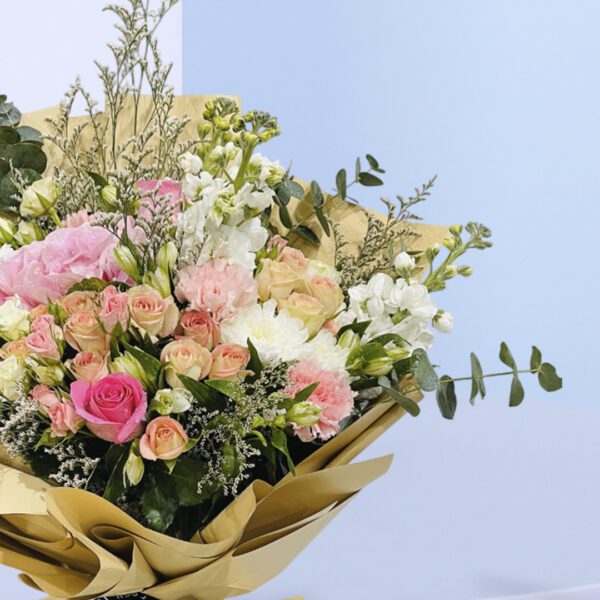 A bouquet of peach and pink roses in a light brown wrap tied with a black ribbon.