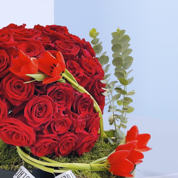 Round flower box with a romantic heart-shaped arrangement of red roses with green accents.