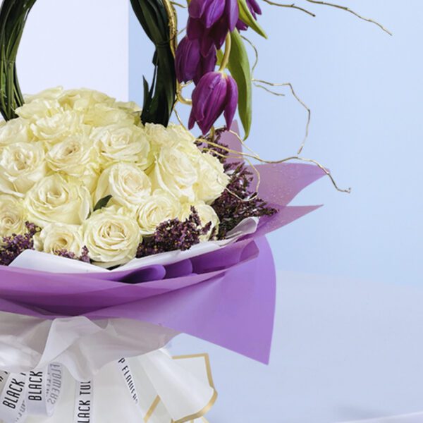 A beautiful arrangement of white roses and purple tulips in a basket with a unique handle.