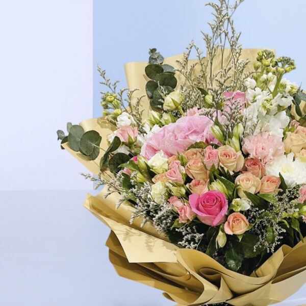 A bouquet of peach and pink roses in a light brown wrap tied with a black ribbon.