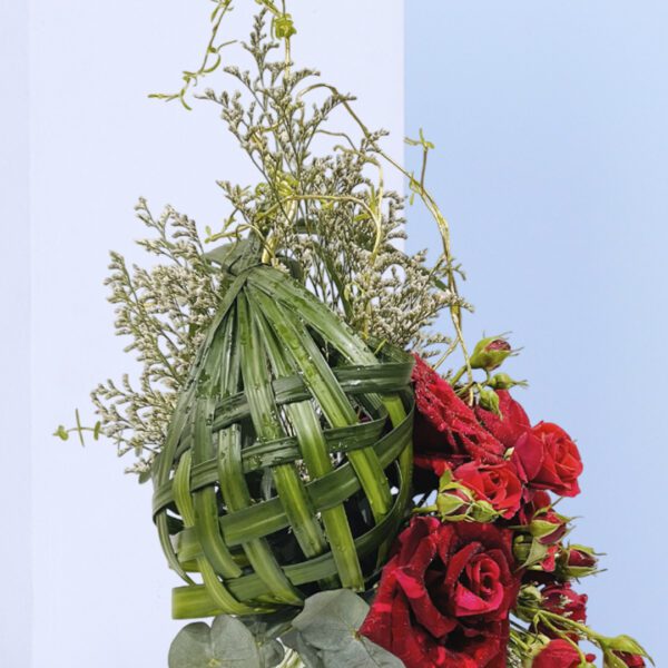 Unique floral arrangement with woven green accents, red roses, and tulips in a glass vase for decor or gifting purposes.