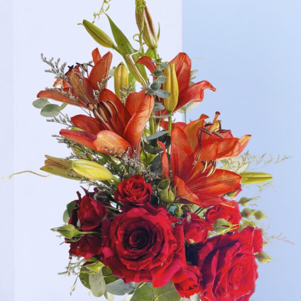 A stunning Valentine's Day floral arrangement with red roses, orange lilies, and lush greenery in a clear glass vase.