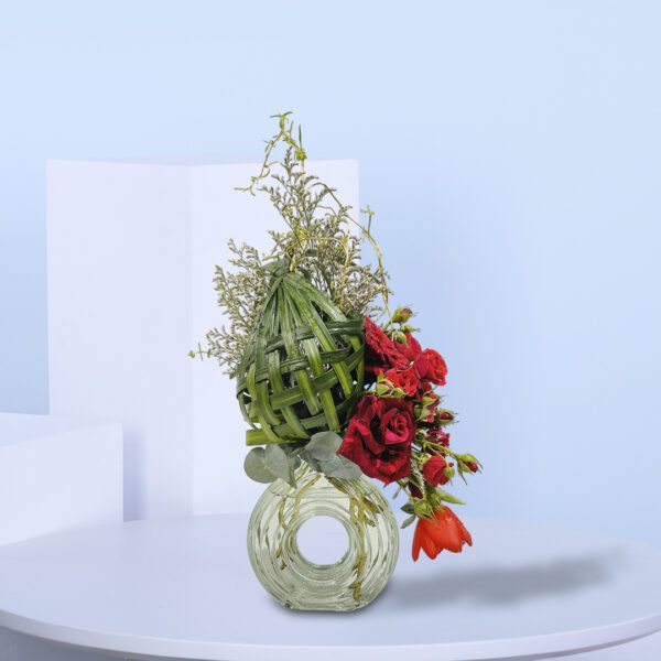 Unique floral arrangement with woven green accents, red roses, and tulips in a glass vase for decor or gifting purposes.