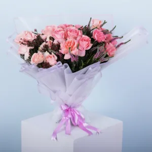 A bouquet of pink roses with other flowers, wrapped in white and pink paper, tied with a pink ribbon, sits on a white pedestal against a light blue background.