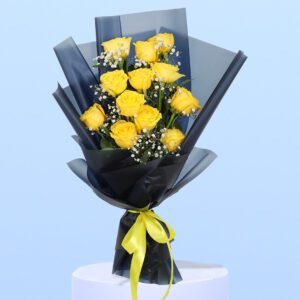 A bouquet of a dozen yellow roses with baby's breath is wrapped in black paper and tied with a yellow ribbon. It sits on a white pedestal against a light blue background.